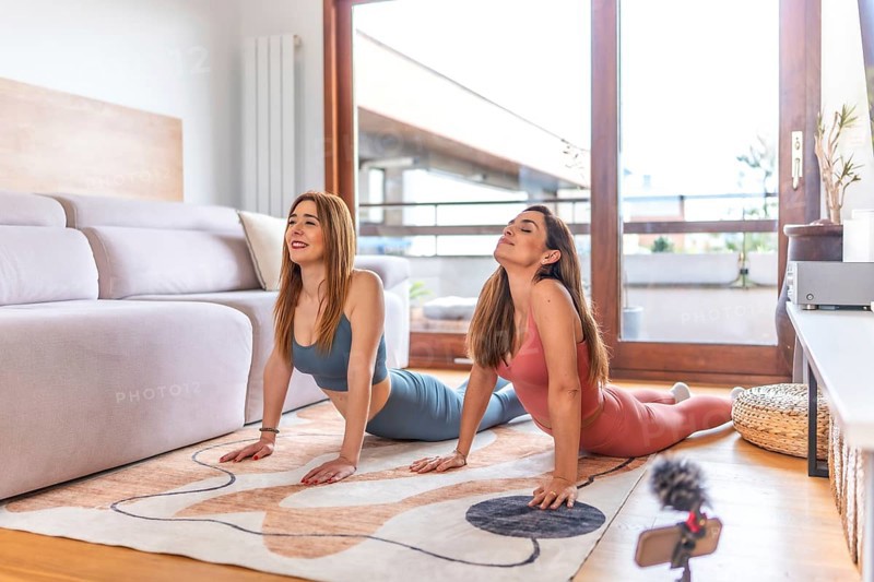 Two young women practicing yoga at home, following an online class on their smartphone during lockdown