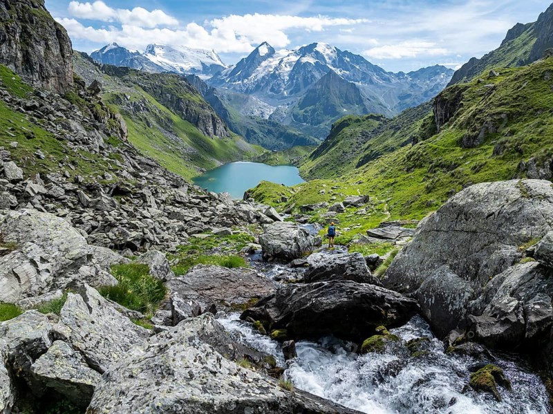 Hiker at the mountain stream and mountain lake Lac de Louvie with glaciated summit of the Grand Combin, Val de Bagnes, Valais, Switzerland, Europe