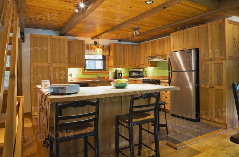 Wooden island with ceramic tile countertop, bar stools and shaker style cabinets in kitchen with lights on inside Canadiana style log cabin home, Quebec, Canada, North America