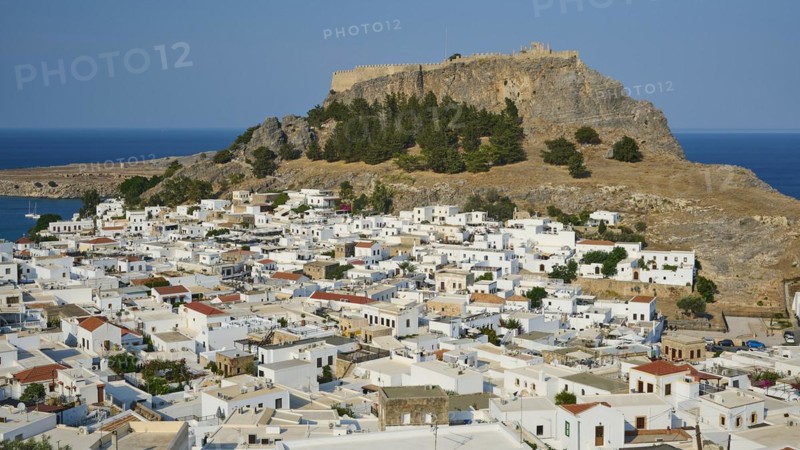 Clear daytime view of a coastal town with traditional Mediterranean architecture under a fortress, Acropolis of Lindos, Lindos, Rhodes, Dodecanese, Greek Islands, Greece, Europe
