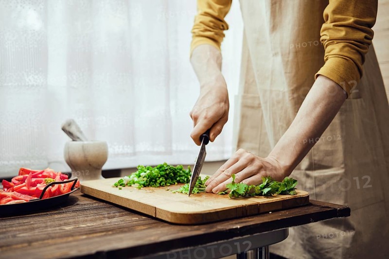 Unrecognizable man chopping cilantro with kitchen knife in the kitchen