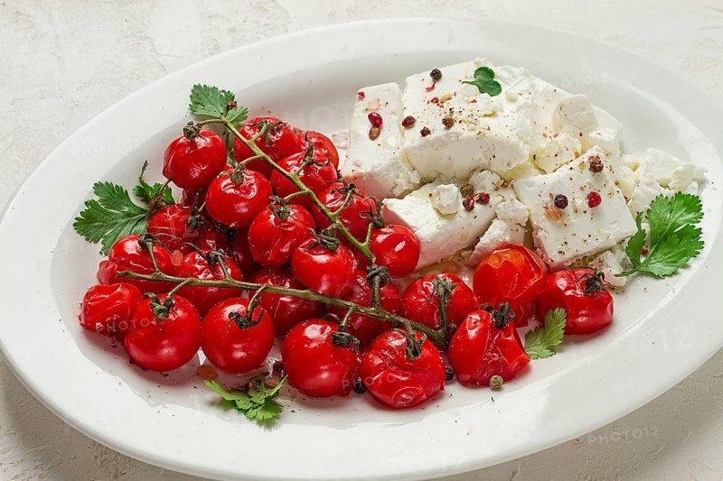 Baked cherry tomatoes, with cheese, and spices, on a white plate, homemade, no people