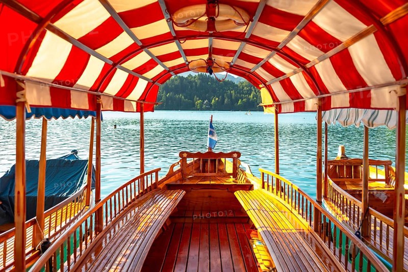 Wooden tourist boat with red and white canopy sailing on lake bled in slovenia, offering scenic view of bled island