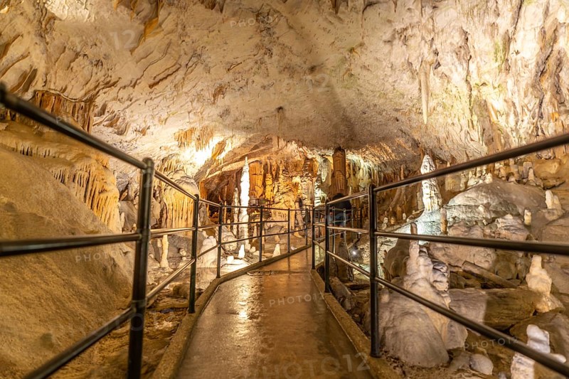 Tourists are enjoying a visit inside postojna cave in slovenia, walking on illuminated footpath surrounded by stalactites and stalagmites