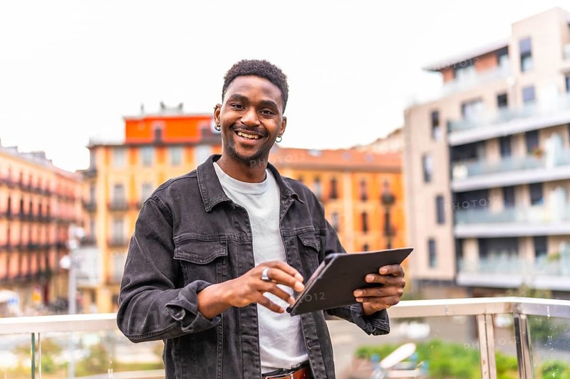 African young man smiling at camera while using digital tablet in the city