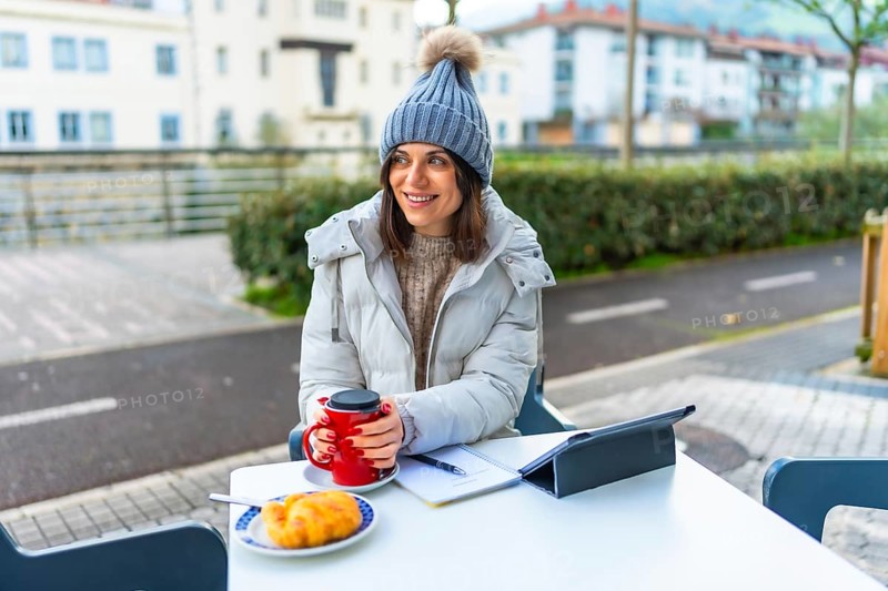 Beauty woman wearing warm clothes and woolly hat warming hands with hot coffee in a sidewalk cafeteria