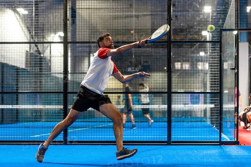 Full length photo of a mature sportive man trying to reach the ball while playing paddle tennis in an indoor court