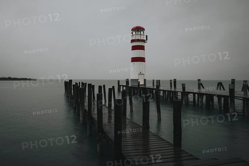 A lighthouse at the end of a wooden jetty under a grey sky over calm water, Podersdorf, Burgenland, Austria, Europe