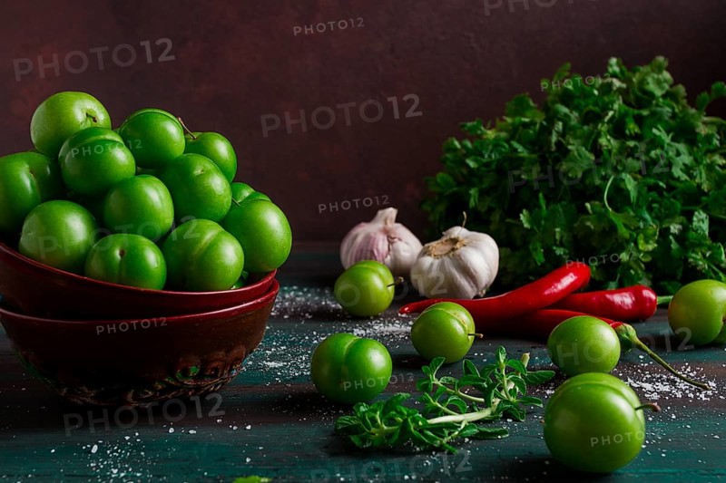 Tkemali, green cherry plum, with ingredients for sauce, cilantro, mint, hot pepper, garlic, on a wooden table, close-up, rustic, food background, no people, selective focus