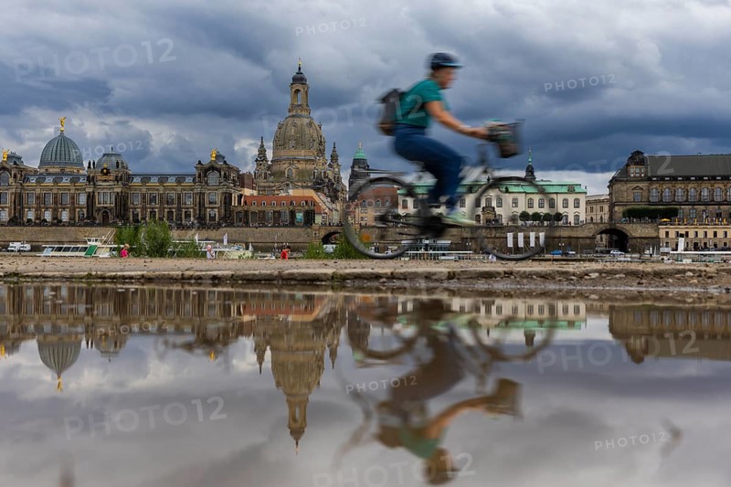 The Dresden silhouette with a cyclist and dark clouds behind the Church of Our Lady is reflected in a puddle on the Elbe cycle path, Elbe cycle path, Dresden, Saxony, Germany, Europe