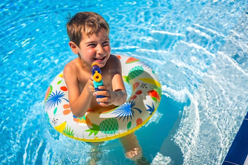 Boy playing with water gun and rubber ring inside the pool