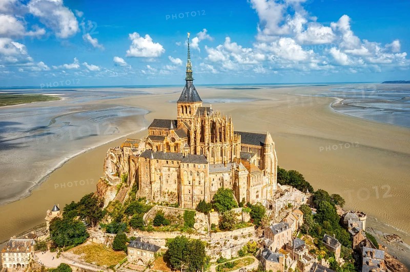 Majestic abbey on an island, surrounded by vast sand, under a clear sky, Le Mont-Saint-Michel