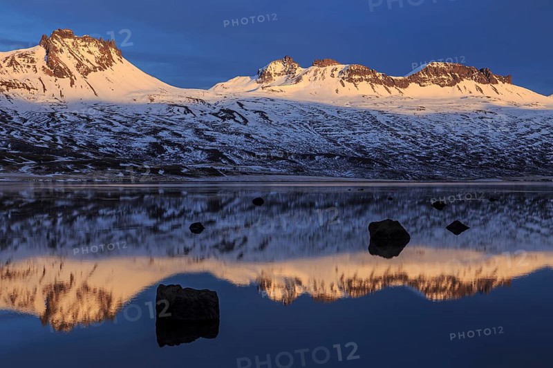 Snow-covered mountains reflected in a fjord in the evening light, Berufjördur, East Fjords, Iceland, Europe