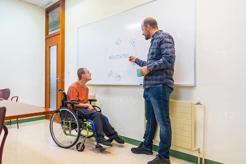 Man with cerebral palsy and colleague using board during brainstorming in a modern coworking