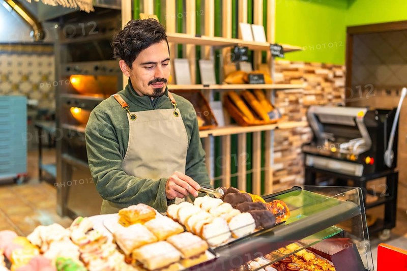 Latin young man arranging sweet artisan pastries on the counter of a bakery shop