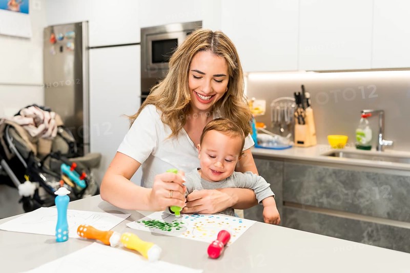 Happy mother and baby boy enjoying creative time together, painting with colorful markers in a bright, modern kitchen