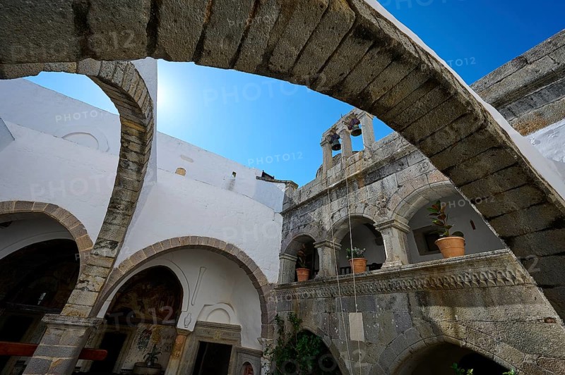 Historic monastery courtyard with stone arches, a tower and hanging plants. Impressive architectural details under a blue sky, Inside the monastery, Agiou Theologou Monastery, Chora, Patmos, Dodecanese, Greek Islands, Greece, Europe