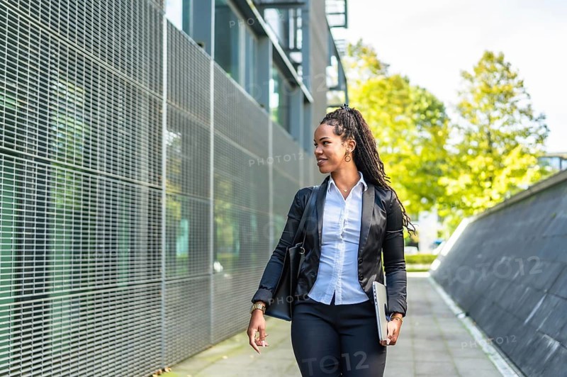 Horizontal photo with copy space of a modern latin businesswoman walking out the block office carrying laptop in a sunny day
