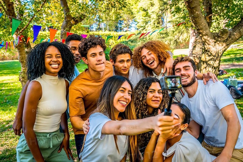 Smiling multi-ethnic friends taking selfie with wearable camera at park while celebrating birthday