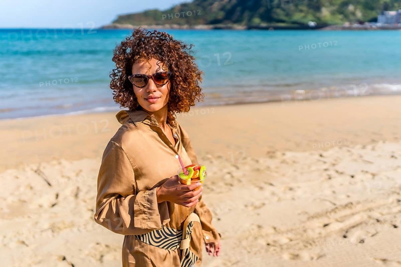 Arab beauty woman in casual summer clothes walking along beach with fresh fruit glass