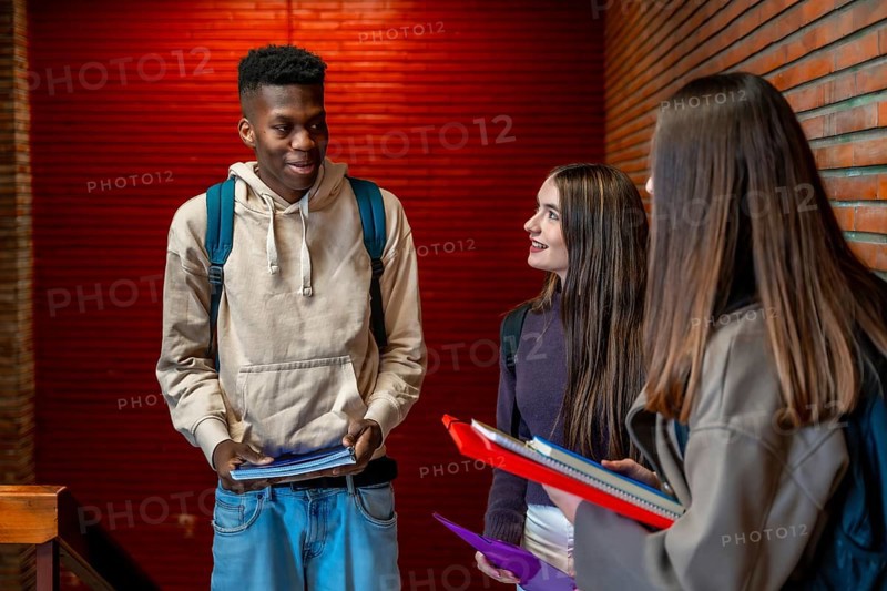 Group of cheerful multi ethnic students talking and smiling together on school hallway during break time