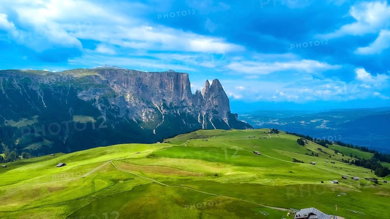 Breathtaking summer landscape featuring lush green meadows, rolling hills, and the majestic peaks of the sassolungo group in the italian dolomites