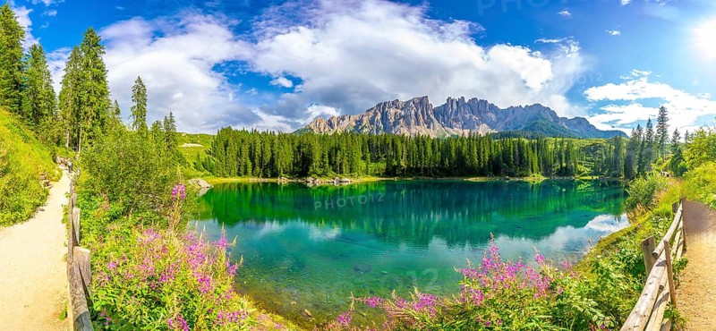 Panoramic view of the beautiful lake carezza with the latemar mountain range in the background on a sunny summer day