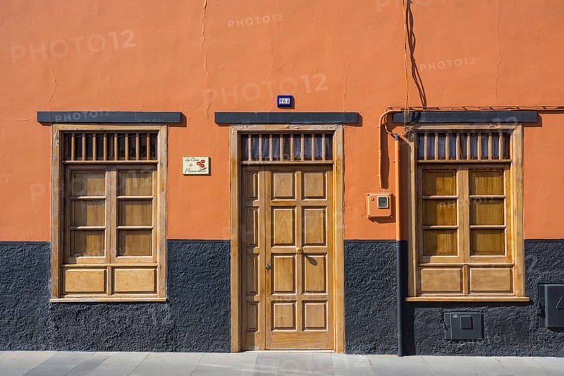A building facade with an orange wall, wooden door, and windows. The base is painted black, creating a minimalistic urban look, Puerto de la Cruz, Tenerife, Canary Islands, Spain, Europe
