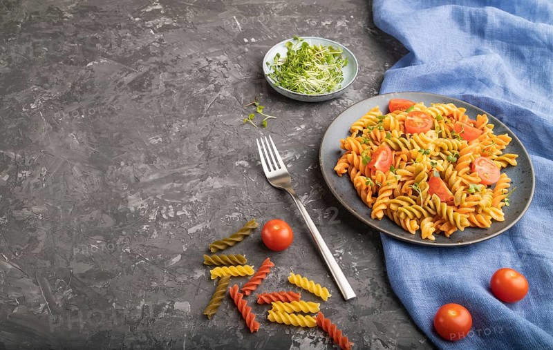 Tortiglioni semolina pasta with tomato and microgreen sprouts on a black concrete background and blue textile. Side view, copy space