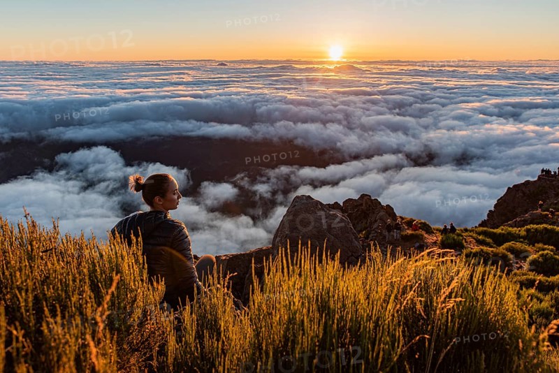 Woman sitting on a mountain watching the sunset over a sea of clouds, Pico Ruivo, Madeira, Portugal, Europe