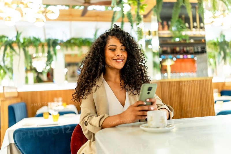 Beauty latin woman using mobile phone sitting on a cafeteria drinking coffee alone