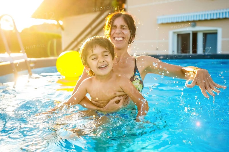 Mother and son are playing and laughing together in a home swimming pool during a sunny summer vacation day