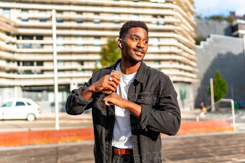 African man listening to music using small wireless earbuds and dancing in the city