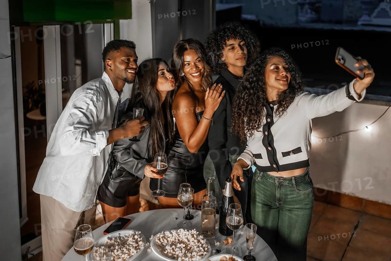 Happy multiracial friends grimacing while taking selfie with cellphone during night roof party