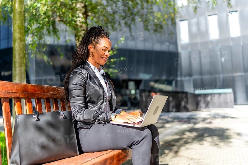 Hispanic elegant businesswoman sitting on city bench working with laptop in the financial district