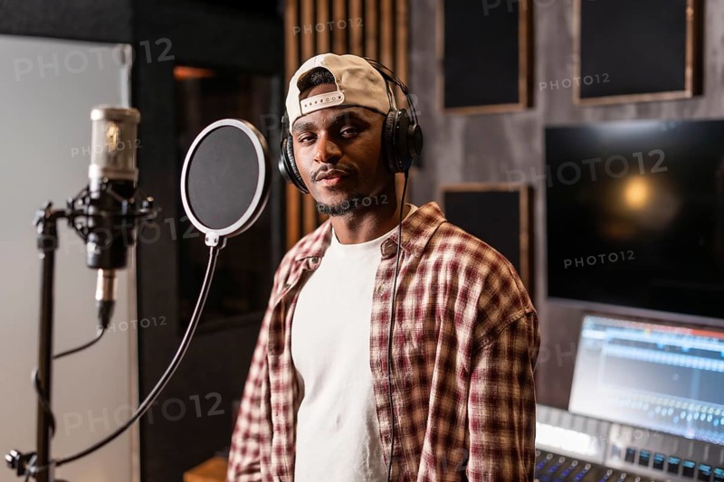 Young african american artist wearing headphones and baseball cap, recording a new album in professional music studio