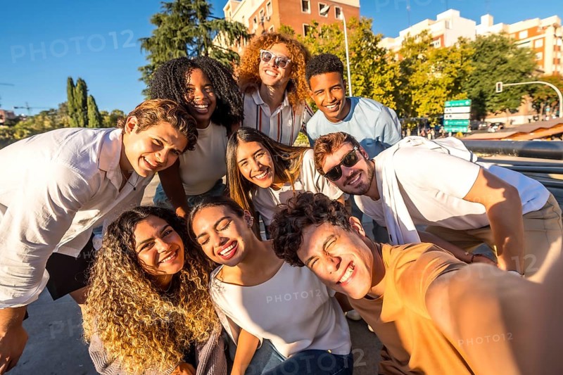 Frontal view of multi-ethnic group of happy friends taking selfie together in the street