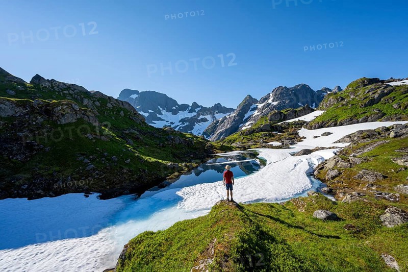 Mountaineer in front of lake with snow remains, Landscape at the mountain hut Trollfjord Hytta, Rocky mountain peaks with snow remains, Mountain landscape at Trollfjord, Lofoten and Vesterålen, Nordland, Norway, Europe