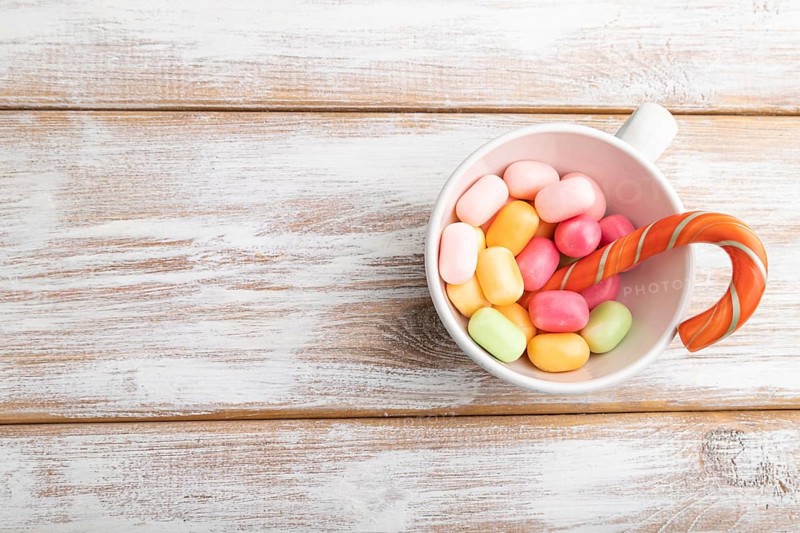 Heap of multicolored caramel candies in cup on white wooden background. copy space, top view, flat lay