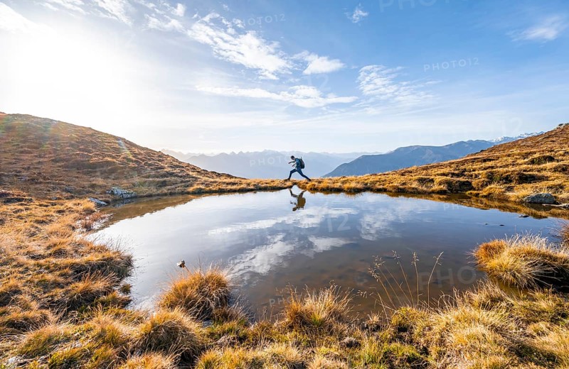 Mountaineer jumping, reflected in a small mountain lake on the Krahberg, mountain panorama in autumn, Venet crossing, Ötztal Alps, Tyrol, Austria, Europe