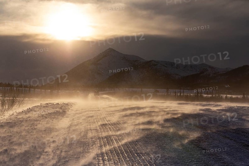 Snow-covered gravel road in the wind in front of mountains, backlight, ice, Dalton Highway, Alaska, USA, North America