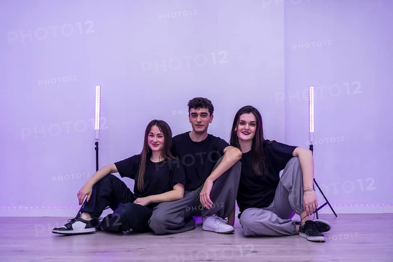 Three young dancers are sitting together on the floor of their dance studio, taking a break and enjoying the purple ambient lighting