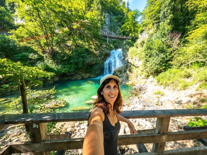 Woman taking selfie with waterfall and turquoise colored water of tolmin gorges in the background, triglav national park, slovenia