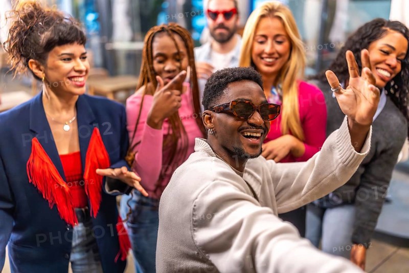 Multi-ethnic friends waving at camera taking selfie during a night party in a bar terrace