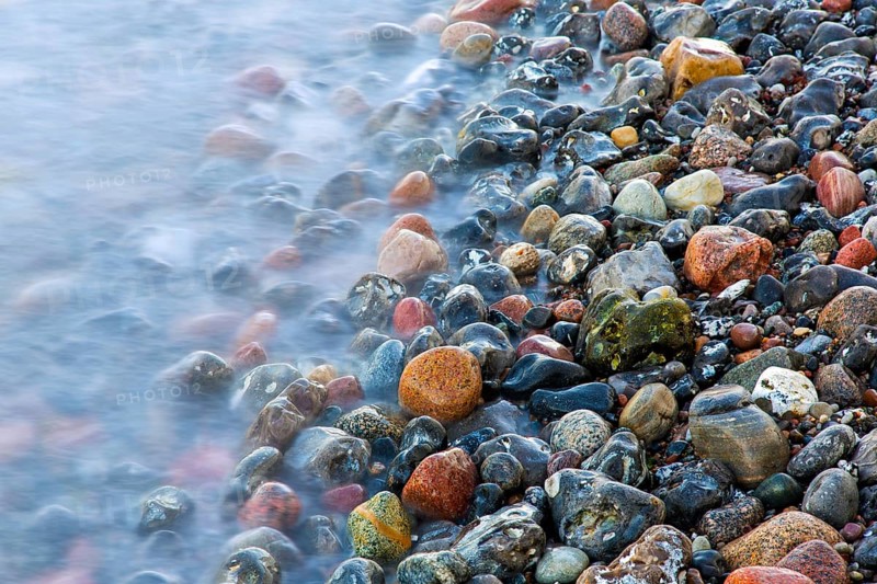 Blurred sea water of wave rolling over wet colourful pebbles on shingle beach, cobble beach