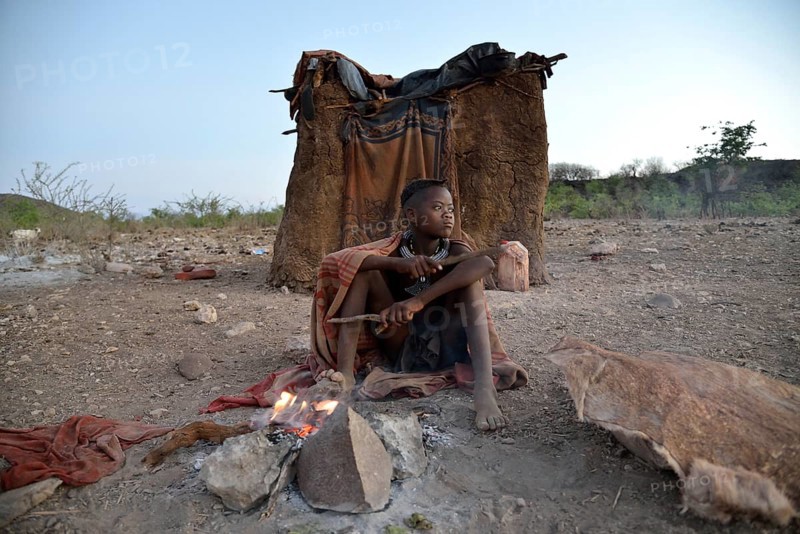 Young shepherdess from the Himba people sitting at a campfire in front of her hut, Ombombo, Kaokoland, Kunene, Namibia, Africa
