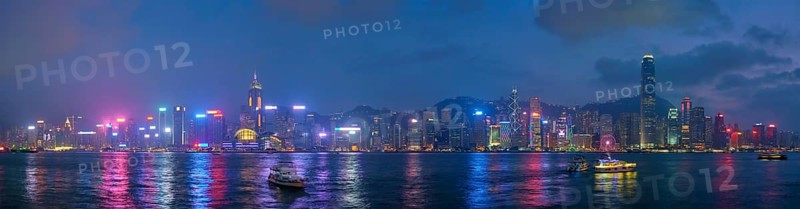 Panorama of Hong Kong skyline cityscape downtown skyscrapers over Victoria Harbour in the evening illuminated with tourist boat ferries, Hong Kong, China, Asia