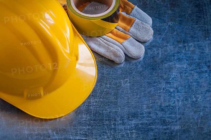 Safety tape yellow building helmet and protective gloves on scratched vintage metallic background construction concept