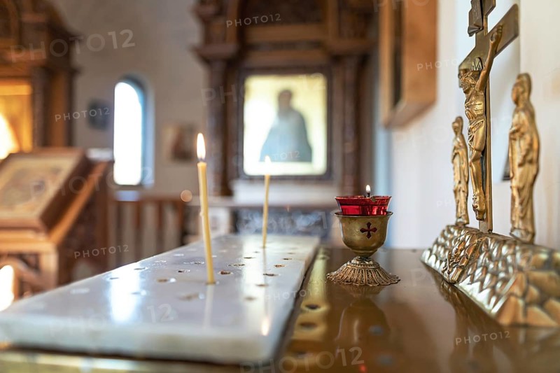 Candles burn in front of the iconostasis and the cross with a crucifix in a small Orthodox chapel