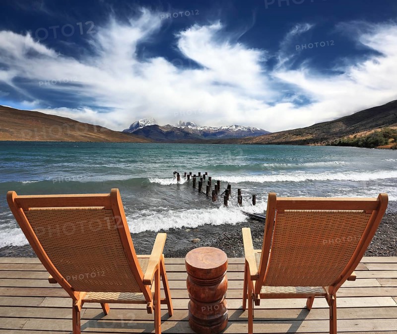 The comfortable place to enjoy the beauty of the lake and clouds in Patagonia. Two folding wooden chairs and a small bedside table on the boardwalk